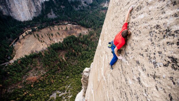 A climber scaling a steep rock face with a scenic forest valley below showcasing climbing