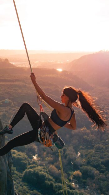 A woman performing climbing high above a forested valley during sunset