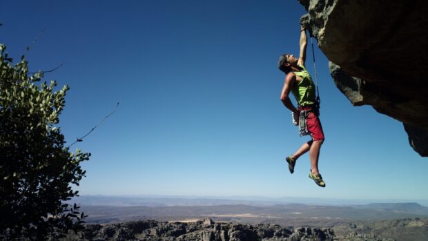 A climber gripping a rock face while climbing outdoors under a clear blue sky