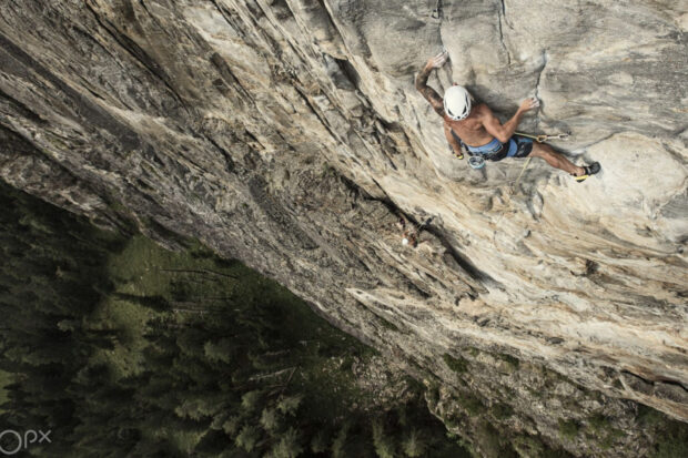 A climber scaling a steep rocky cliff with safety ropes and helmet in a mountain environment