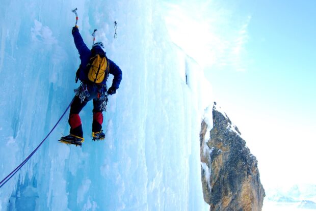 A climber using ice axes and crampons climbing a frozen ice wall
