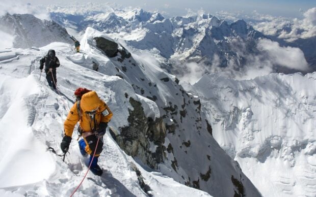 Experienced climbers ascending a snow covered mountain ridge in high altitudes