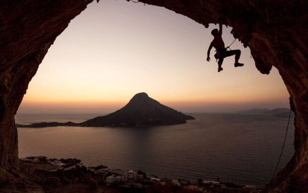 A climber scaling a rock over a coastal landscape at sunset