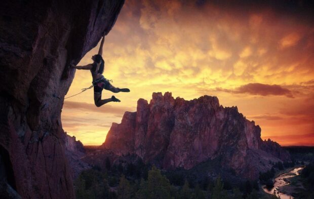 A climber scaling a steep rock face during sunset in a mountainous landscape