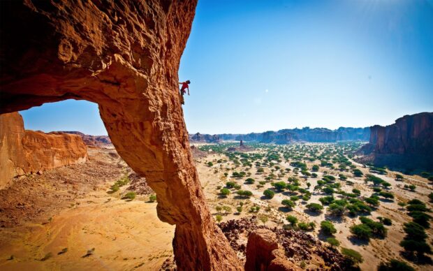 A climber scaling a steep rock formation in a desert landscape with clear blue sky