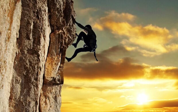 A climber ascending a steep rock during a sunset climb