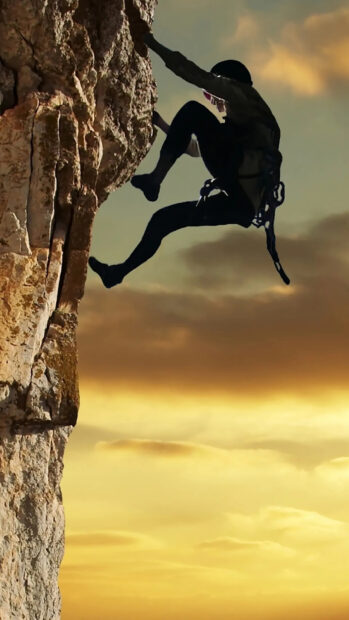 A climber scaling a steep rock face during sunset with climbing gear