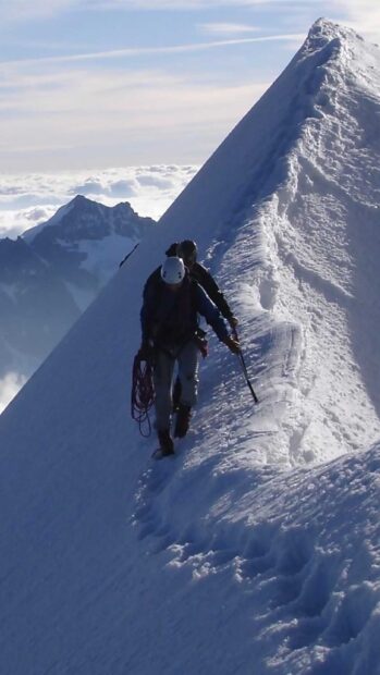 Two climbers ascending a steep snowy mountain ridge during an alpine climb