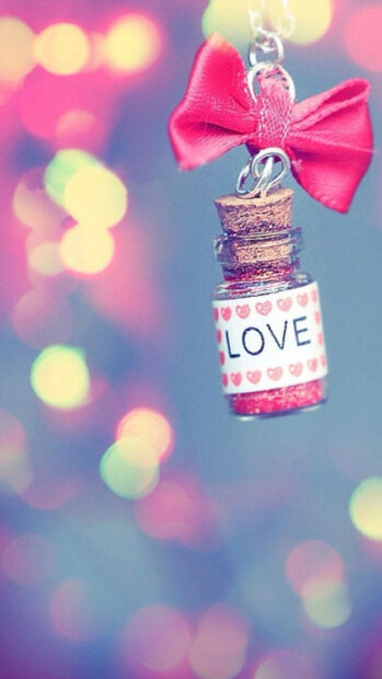 A love message charm bottle with a pink bow hanging on a blurred colorful background