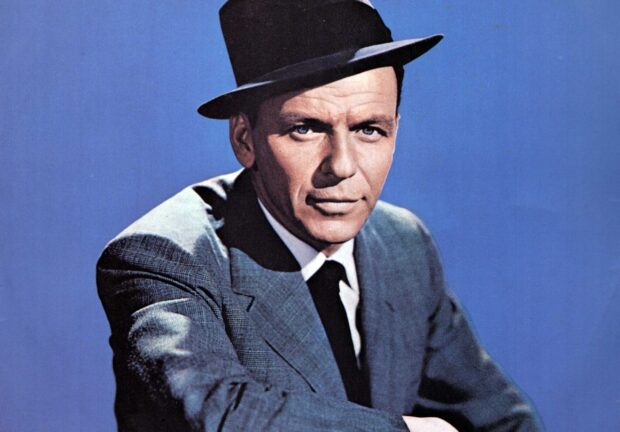Frank Sinatra wearing a hat and suit posing against a blue background