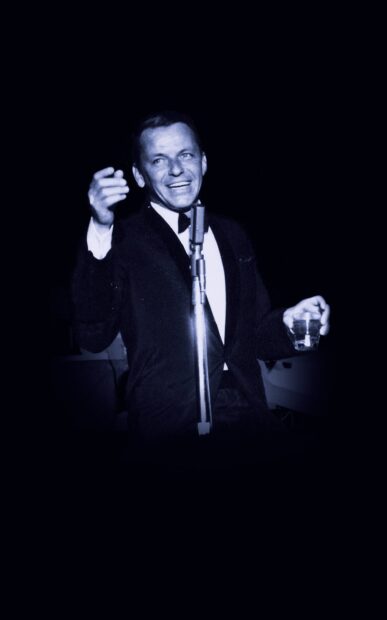 Frank Sinatra enjoying a drink and smiling while performing live on stage