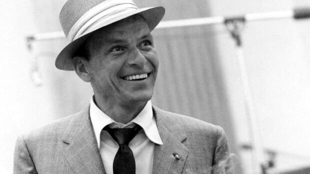 Frank Sinatra smiling wearing a hat and suit in a classic vintage setting