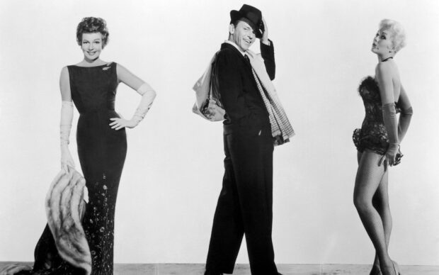 Frank Sinatra standing between two glamorous women in vintage fashion in black and white photograph