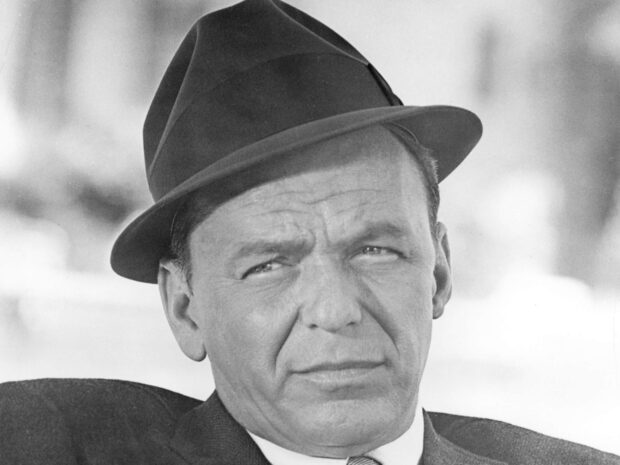 Frank Sinatra wearing a fedora hat with a serious expression in a classic black and white portrait