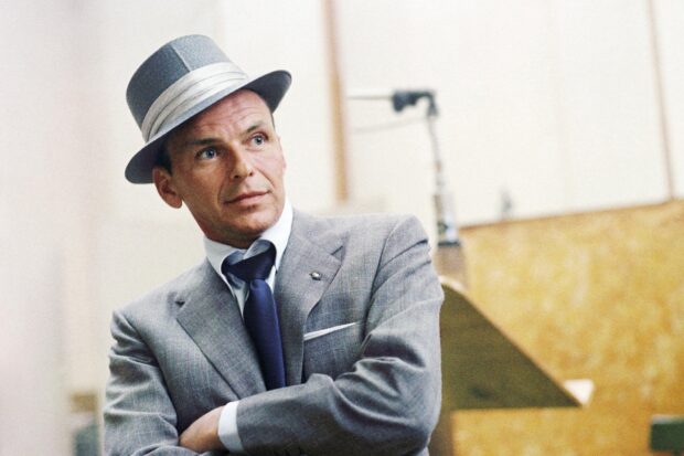 Frank Sinatra wearing a gray suit and hat looking thoughtful in a studio setting