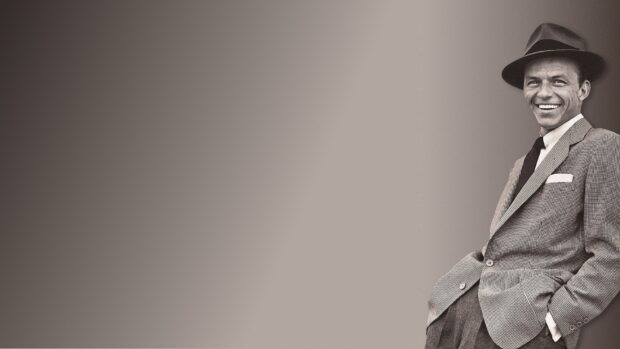 Frank Sinatra wearing a hat and suit smiling while leaning against a neutral background