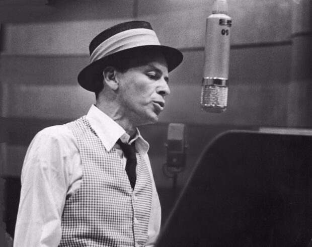 Frank Sinatra wearing a hat and vest singing into a microphone in a recording studio
