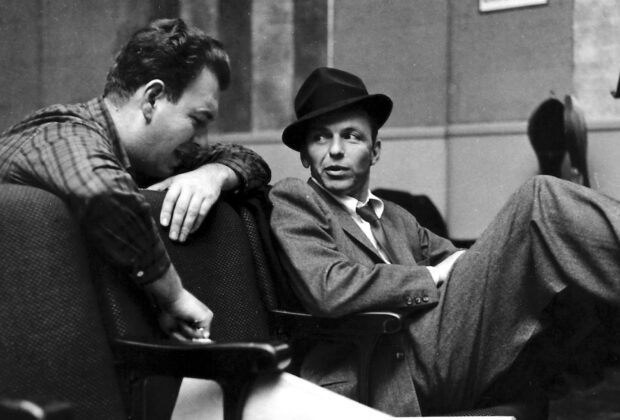 Frank Sinatra casually sitting and talking with a man in a vintage setting