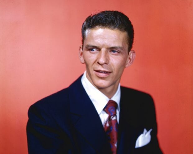 Young Frank Sinatra wearing a suit and tie with a red background