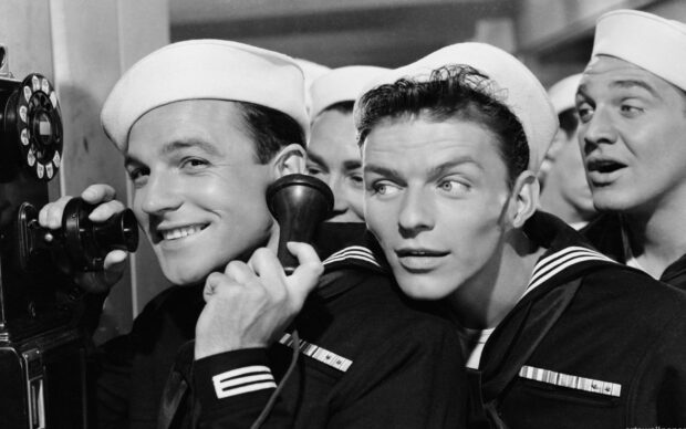 Frank Sinatra in navy uniform making a call on a vintage phone with sailors around him