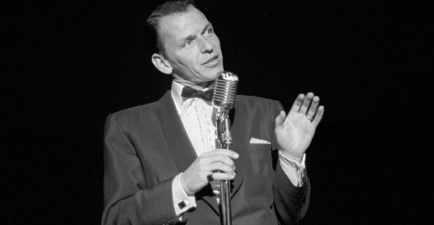 Frank Sinatra is performing on stage with a vintage microphone in a classic suit