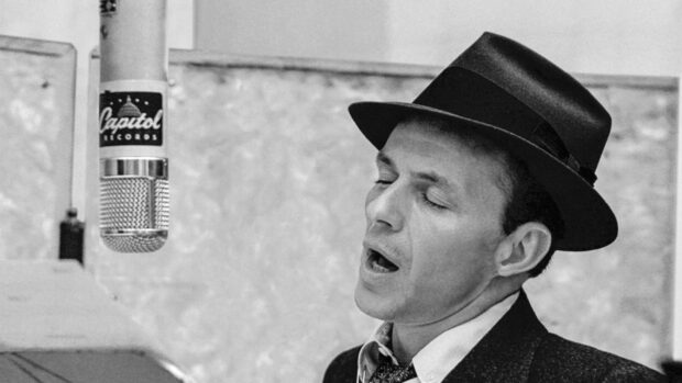 Frank Sinatra singing passionately in a recording studio wearing a hat
