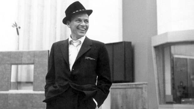 Frank Sinatra smiling in a suit and hat in a vintage indoor setting
