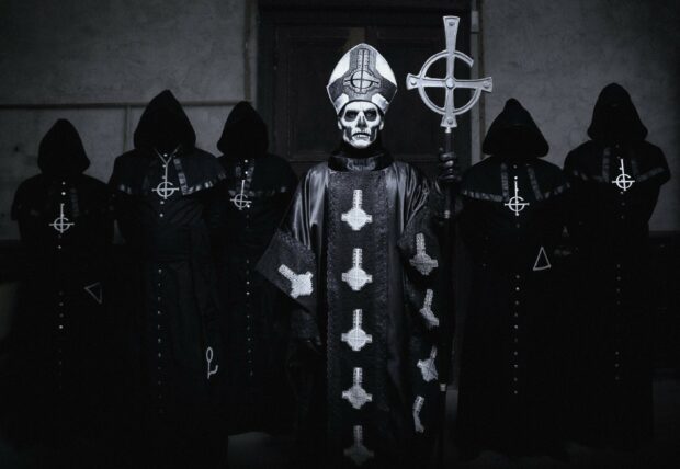 Ghost Band members dressed in dark robes with a skeletal figure holding a staff standing in the center