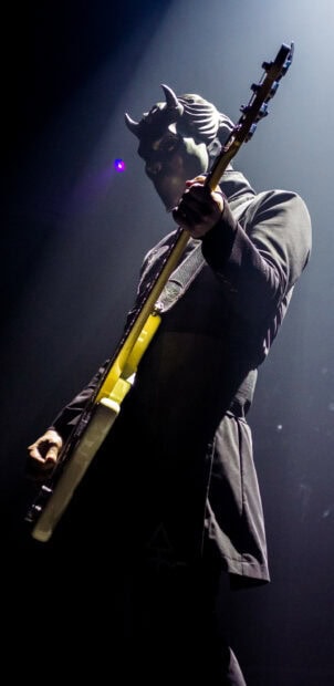 Musician wearing a devil mask playing guitar on stage during a live concert