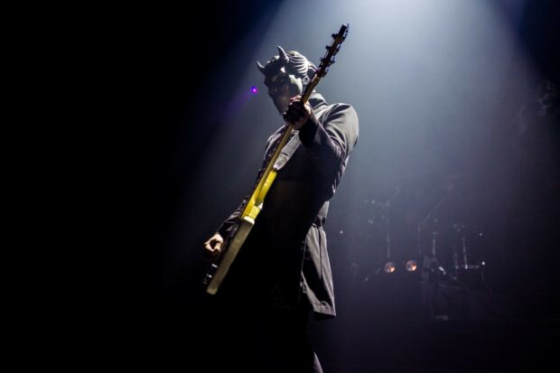 A Ghost Band musician performing on stage playing guitar in a dark concert setting