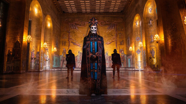 Ghost Band member dressed in ornate robes standing in a golden hall with smoke around