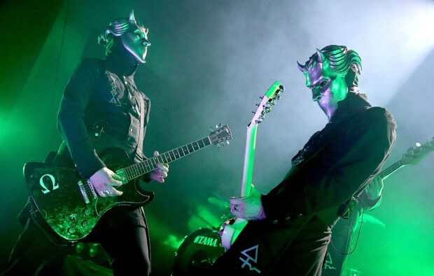 Two ghost band members wearing masks and playing guitars on stage with green lights
