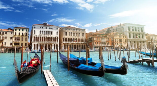 Ancient gondola docked in turquoise water near old Venice buildings on a sunny day