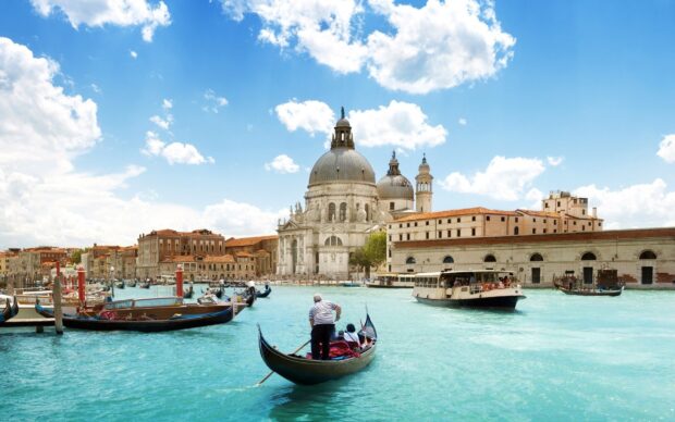 Gondola moving through Venice canal with historic buildings and a clear blue sky