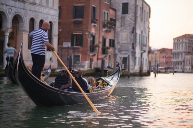 Gondola navigating a calm canal with historic buildings in Venice at sunset