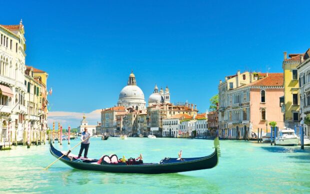 A gondola gliding through Venetian canals with historic buildings and a bright blue sky background