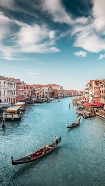 Venice gondola cruising through historic canal with colorful buildings alongside and blue sky