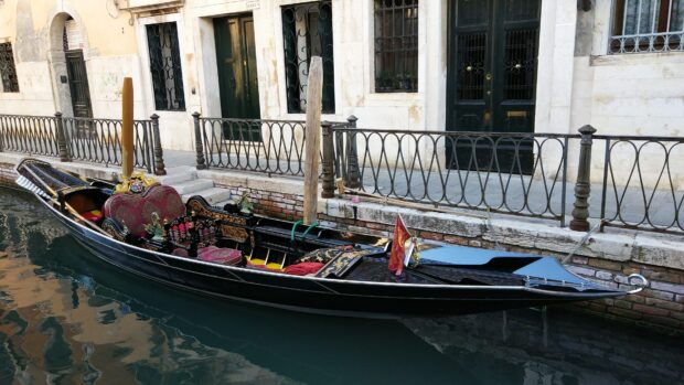 Elegant gondola moored along a canal with ornate seating and vintage architecture in the background