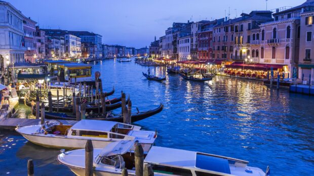 Evening view of gondola boats lined up on the Venetian canal with city lights reflecting on the water