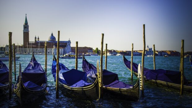 Gondolas docked on the water with a cityscape and church tower in the background
