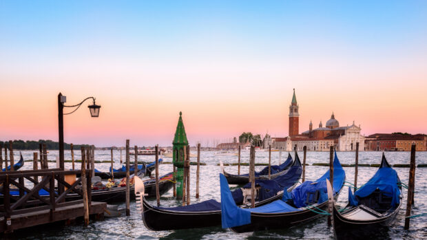 Gondola lined up at the dock in Venice during sunset with historic buildings in the background