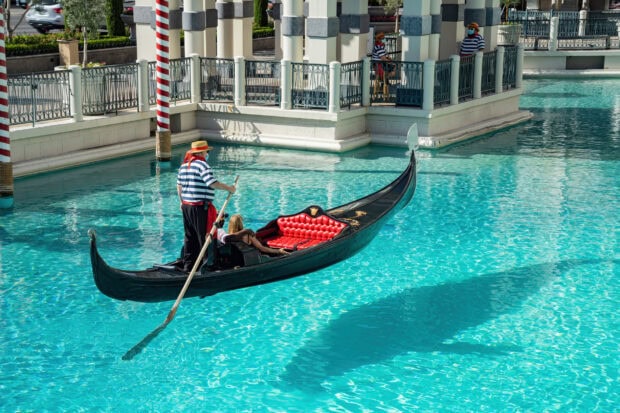 Gondola man rowing with passenger on a bright sunny day in clear water canal