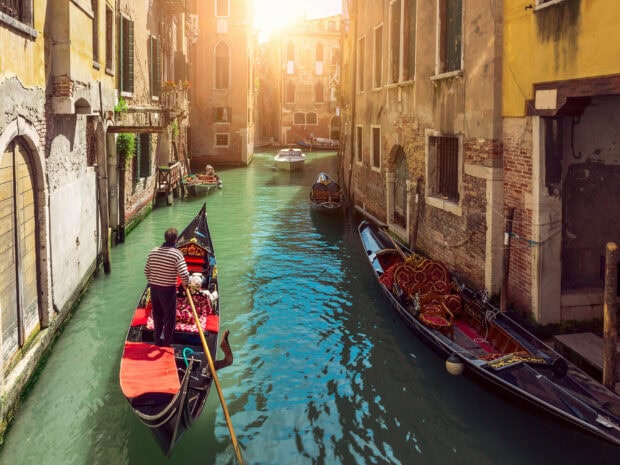Gondolier rowing a gondola through a narrow canal in Venice with historic buildings on both sides