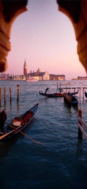 Gondola floating on water with Venice buildings in the background at sunset
