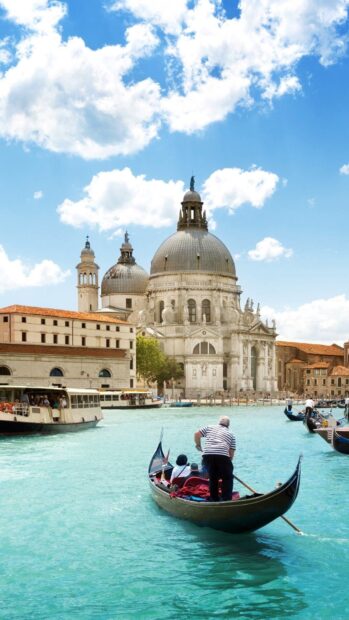 Gondola with tourists floating on canal near historic cathedral in Venice