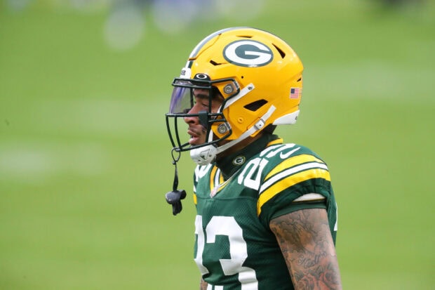 A Green Bay Packers player wearing a yellow helmet and green jersey with tattoos on his arm