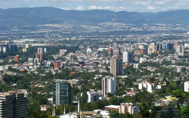 A panoramic view of Guatemala City with modern buildings and surrounding mountains in clear daylight