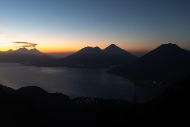 Silhouettes of Guatemala volcanoes at dusk with a glowing orange sky over the lake