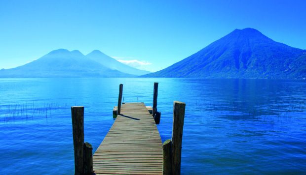 A wooden pier extending over lake with Guatemala volcanoes in the background