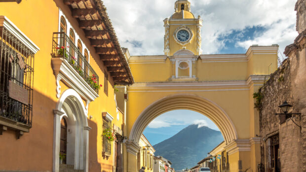 Antigua Guatemala street with a clock tower arch and volcano in the background
